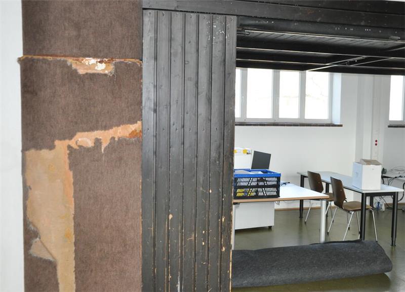 Blick durch eine Tür mit abblätternder Farbe auf einen Raum mit Tischen, Stühlen und Computern