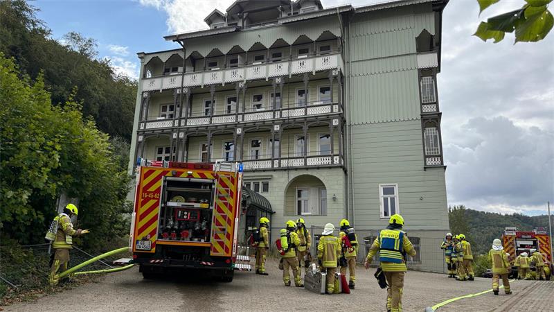 Feuerwehrleute und ein Feuerwehrfahrzeug vor einem Holzgebäude.
