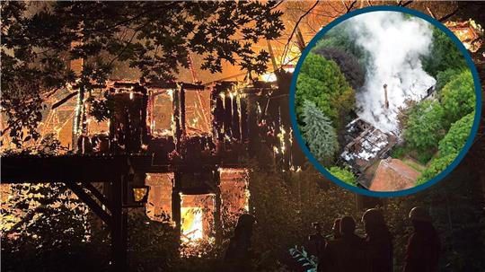 Zusehen sind zwei Feuerwehrmänner in voller Montur, die auf ein brennendes Gebäude schauen.