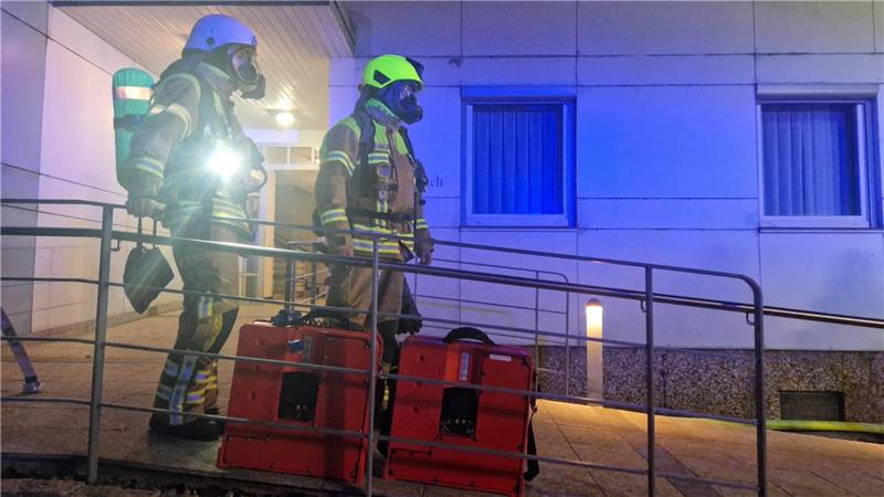 Feuerwehrmänner kommen mit Atemschutzmasken aus dem Hauseingang. 