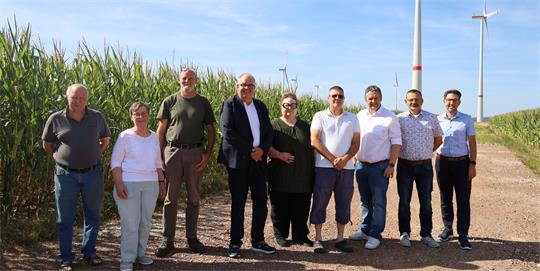 Gruppe von neun Personen steht auf einem Feldweg vor Windrädern bei klarem Himmel