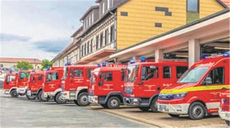 Vor Garagen stehen in Reihe die Fahrzeuge einer Feuerwehr.