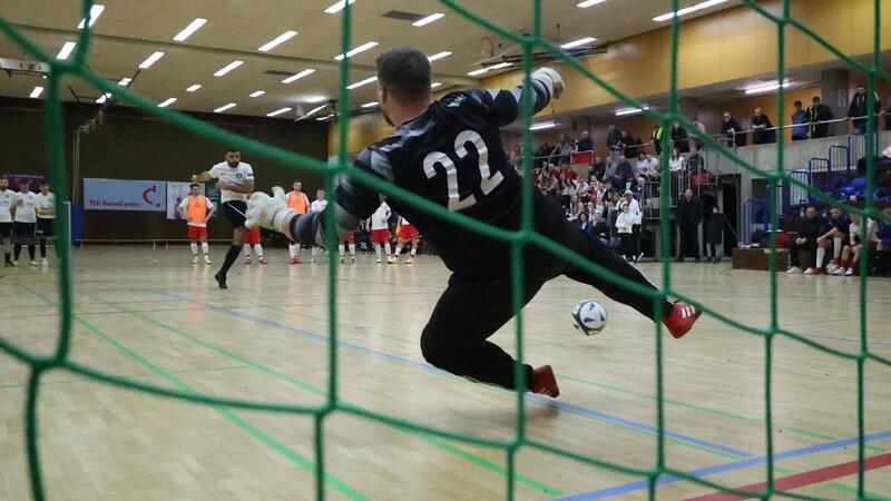 Ein Fußballer schießt in der Halle einen Siebenmeter auf das Tor.