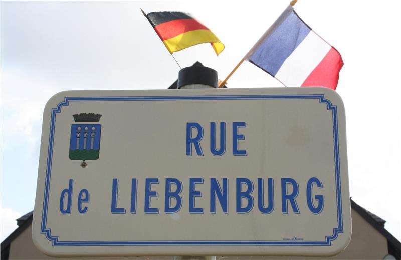  Straßenschild, gerahmt von deutscher und französischer Nationalflagge 