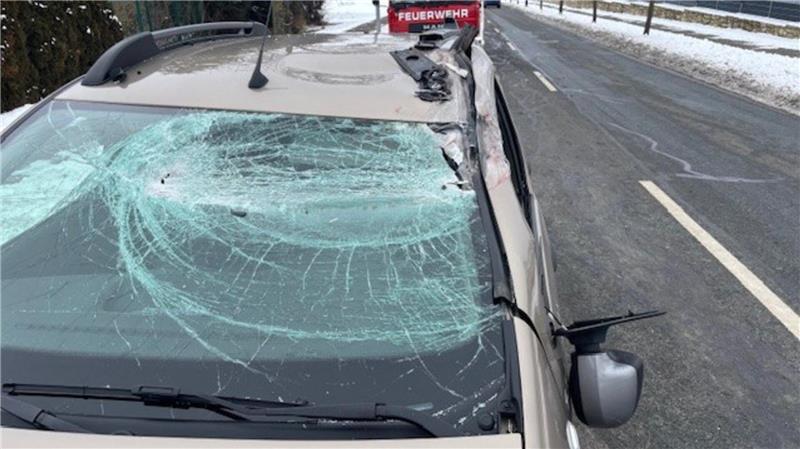 Auto mit stark zertrümmerter Windschutzscheibe steht auf schneebedeckter Straße, im Hintergrund Feuerwehrfahrzeug
