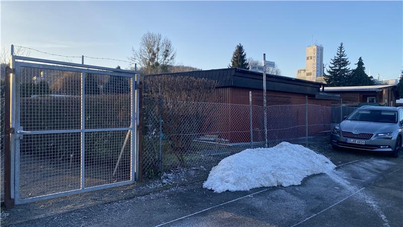 Gartenpazellen hinter einem Zaun. Im Hintergrund ist Gebäude der Firma zu sehen, dem die Fläche gehört.