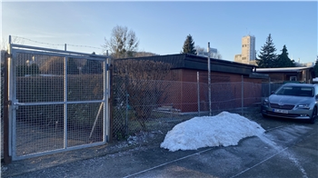 Gartenpazellen hinter einem Zaun. Im Hintergrund ist Gebäude der Firma zu sehen, dem die Fläche gehört.