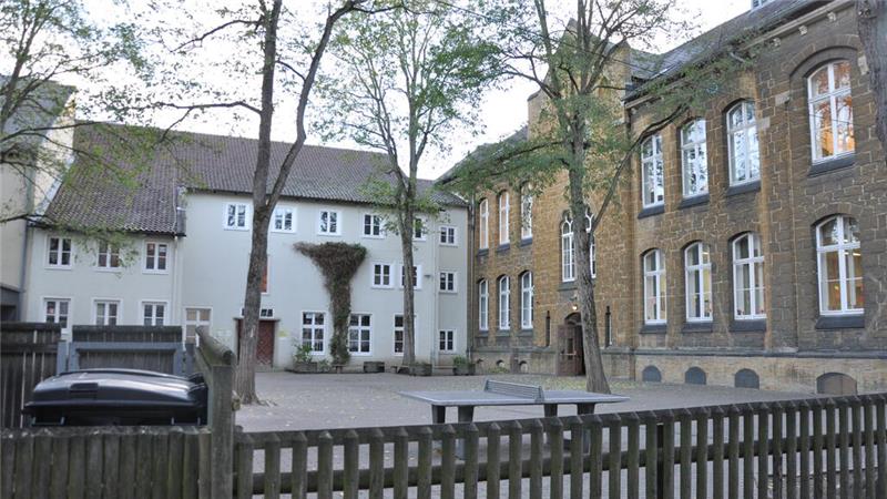 Hof mit Tischtennisplatte, Bänken und Bäumen vor zwei mehrstöckigen Gebäuden mit vielen Fenstern