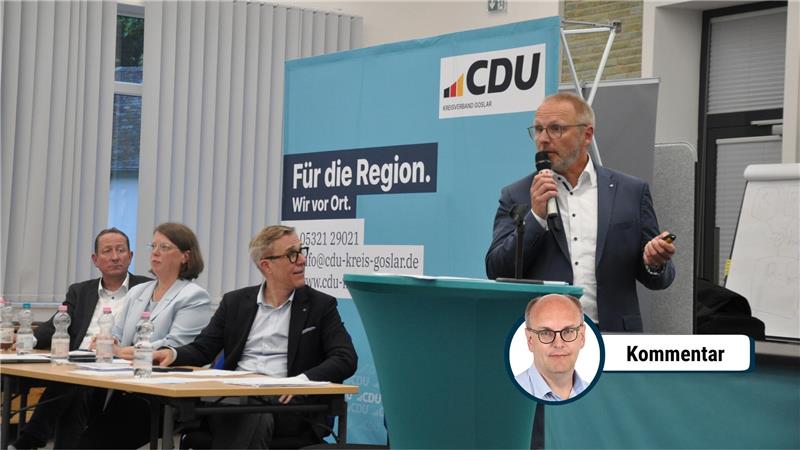 Vier Personen sitzen an einem Tisch, eine Person steht mit Mikrofon vor einem CDU-Banner und hält eine Präsentation