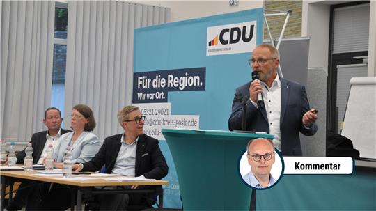 Vier Personen sitzen an einem Tisch, eine Person steht mit Mikrofon vor einem CDU-Banner und hält eine Präsentation