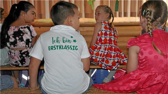 Vier Kinder sitzen auf einer Bank, eines trägt ein weißes T-Shirt mit der Aufschrift 'Ich bin ERSTKLASSIG'