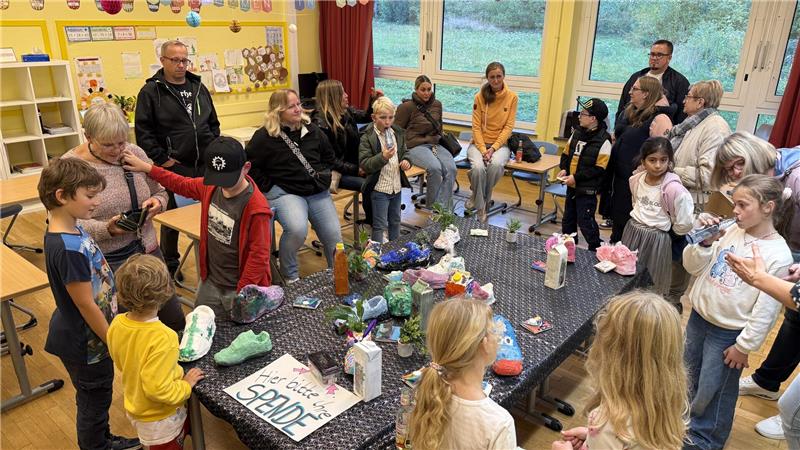 Kinder und Leher stehen und sitzen in einem Raum in der Grundschule.
