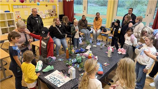 Kinder und Leher stehen und sitzen in einem Raum in der Grundschule.