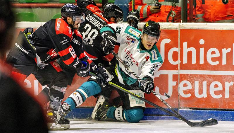 Zwei Eishockeyspiel in schwarzen Trikots und ein Eishockeyspieler im weißen Trikot kämpfen um den Puck.