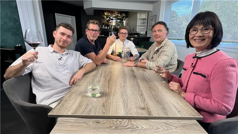 Fünf Personen sitzen an einem Tisch und schauen in die Kamera