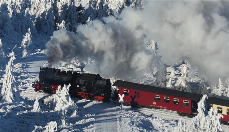 Ein Zug fährt durch eine verschneite Winterlandschaft und kreuzt einen Weg.