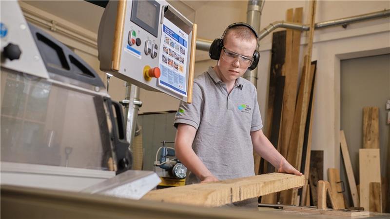 Ein auszubildener Tischler schneidet Holz an einer Maschine.
