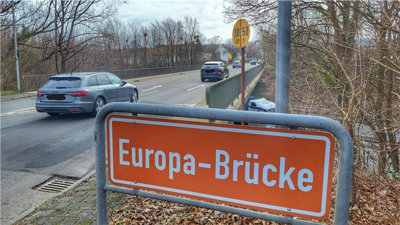 Straßenszene mit orangefarbenem Straßenschild 'Europa-Brücke' an einer Brücke, auf der Autos fahren