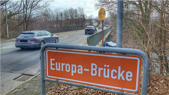 Straßenszene mit orangefarbenem Straßenschild 'Europa-Brücke' an einer Brücke, auf der Autos fahren