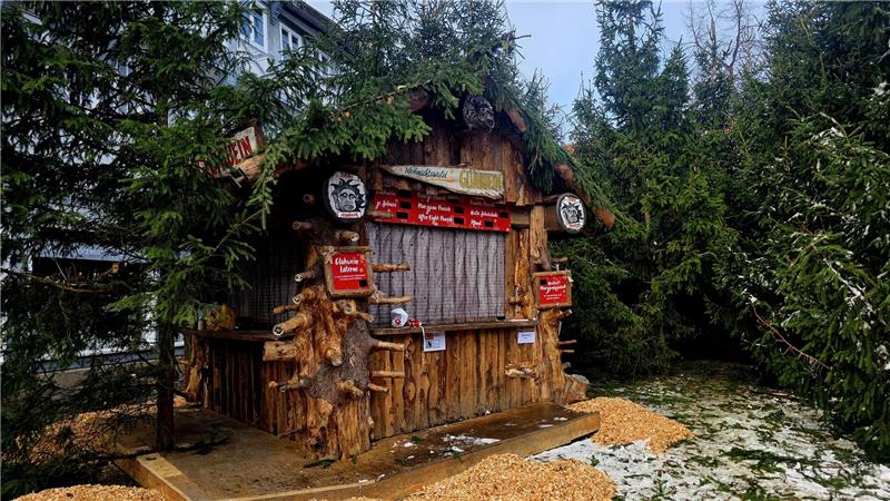 Weihnachtsmarkt Goslar: Öffnungszeiten, Parken und Co. Holzhütte mit Tannenzweigen auf dem Dach umgeben von Tannenbäumen und Holzspänen auf dem Boden.