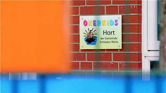 Schild mit bunter Aufschrift 'OKERKIDS' und Text 'Hort der Gemeinde Schladen-Werla' an roter Backsteinwand neben weißem Fensterrahmen