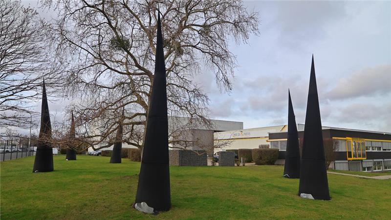 Auf der Wiese eines Gewerbegebietes stehen einige mehrere Meter hohe schwarze "Hütchen".