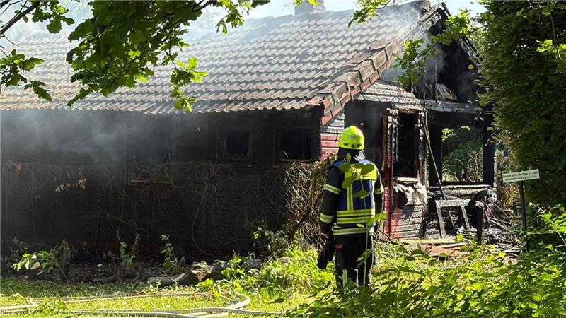 Ein Feuerwehrmann steht vor der zerstörten und ausgebrannten Hütte.