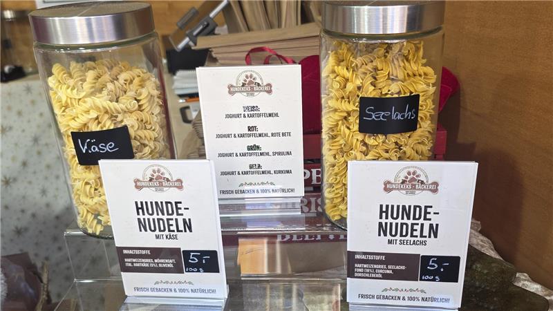 Herzförmige und stangenförmige Lebkuchen auf einem Marktstand, teilweise in einer Tasse mit Hundemotiv, mit Preisschildern und braunen Papiertüten im Hintergrund.