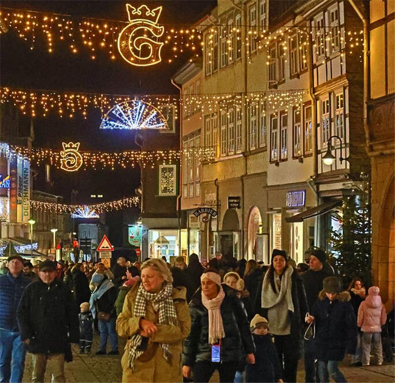 Am Super-Samstag kommen Besucher aus ganz Deutschland Weihnachtlich beleuchtete Altstadtstraße mit mehreren Gruppen von Menschen, beleuchtete Kronen- und G-Symbole hängen über der Straße.