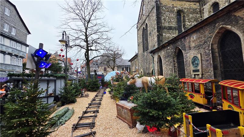 Weihnachtlich geschmückter Außenbereich mit Miniatureisenbahn, Tannenbäumen und einer lebensgroßen Rentierfigur neben einer alten Kirche.