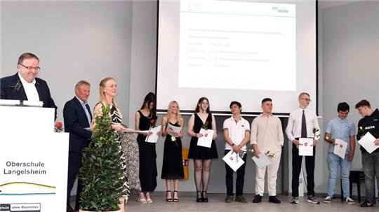 Die Klasse 10c mit Klassenlehrerin Jasmin Schmidt bei der Zeugnisübergabe. Schulleiter Klaus Scheller ruft die Namen der Schüler auf. Dahinter gratuliert auch der stellvertretende Schulleiter Joachim Kausch.