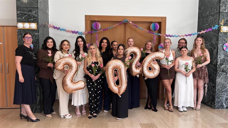 Absolventen aus fünf Klassen feierlich verabschiedet Mehrere Frauen und ein Mann stegen nebeneinander, sie halten jeweils eine Blume und die Ziffern für 2026 in der Hand.