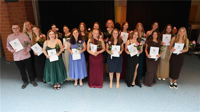 Viele Frauen und ein Mann stehen mit einer Urkunde und einer Blume in der Hand nebeneinander.