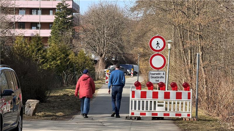 Das Foto zeigt zwei Fußgänger, die auf einer durch Schilder gesperrten Straße unterwegs sind.
