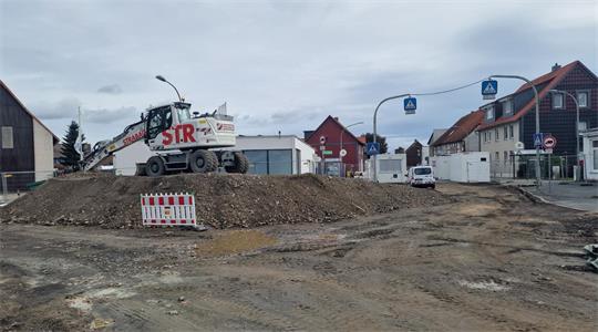 Baustelle mit Erdhügel, Bagger und Absperrung in einer Wohnstraße mit Häusern und parkenden Autos
