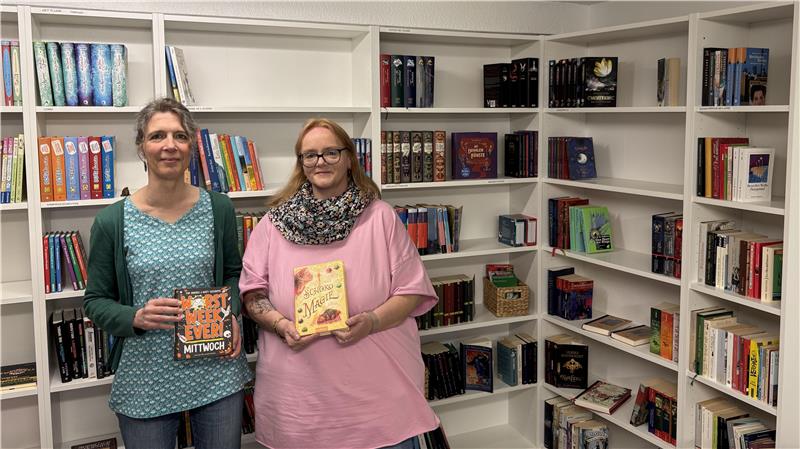 Zwei Frauen stehen vor einem Bücherregal und halten Bücher in der Hand.