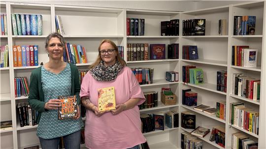 Zwei Frauen stehen vor einem Bücherregal und halten Bücher in der Hand.