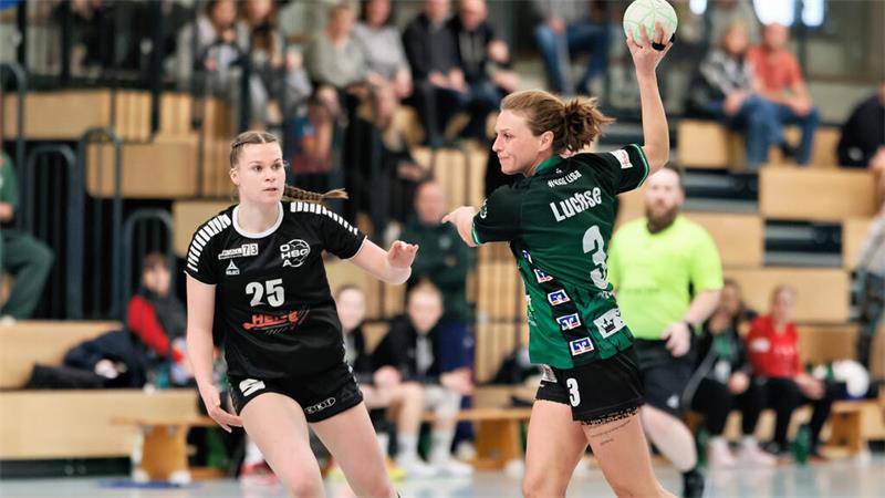 Zwei Handballspielerinnen in Aktion, eine mit Ball in Wurfhaltung, die andere in Verteidigungsposition