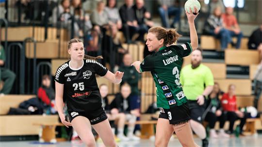 Zwei Handballspielerinnen in Aktion, eine mit Ball in Wurfhaltung, die andere in Verteidigungsposition