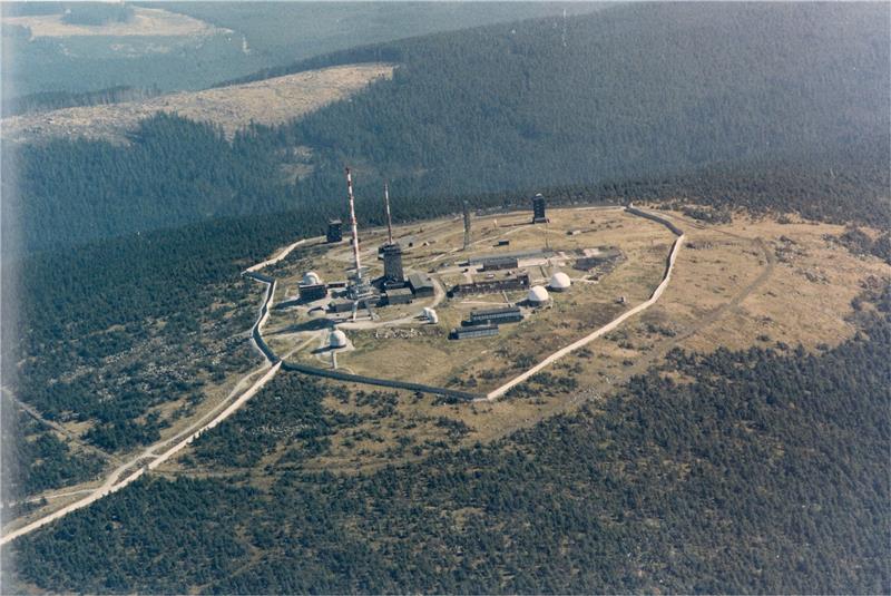 Reise in die Zeit des Kalten Kriegs: Spionage im Harz Die Luftaufnahme entstand aus einem Hubschrauber des Bundesgrenzschutzes und zeigt das Brockenplateau Ende der 1980er Jahre. Wie Pilze scheinen die Radome aus dem Boden zu schießen – die Kuppeln beherbergen die Spionagetechnik. Umfasst ist die Kuppe von einer Mauer. Foto: BGS-Archiv/Heimatmuseum Abbenrode