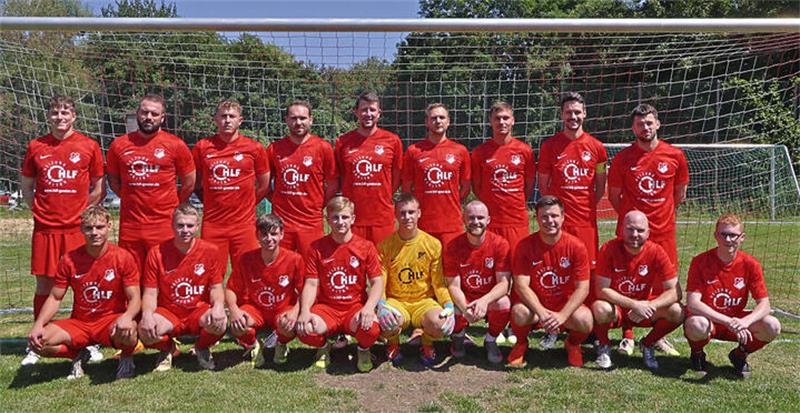 Mannschaftsfoto einer Fußballmannschaft mit 16 Spielern in roten Trikots vor einem Fußballtor auf einem Rasenplatz bei Sonnenschein
