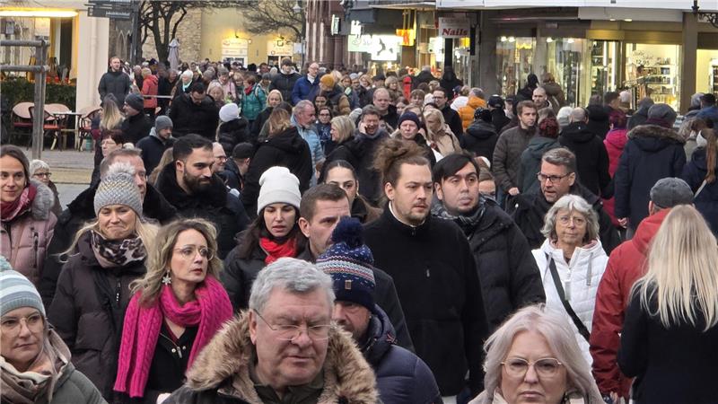 Menschenmenge auf einer belebten Einkaufsstraße mit Geschäften und Straßencafés im Hintergrund.