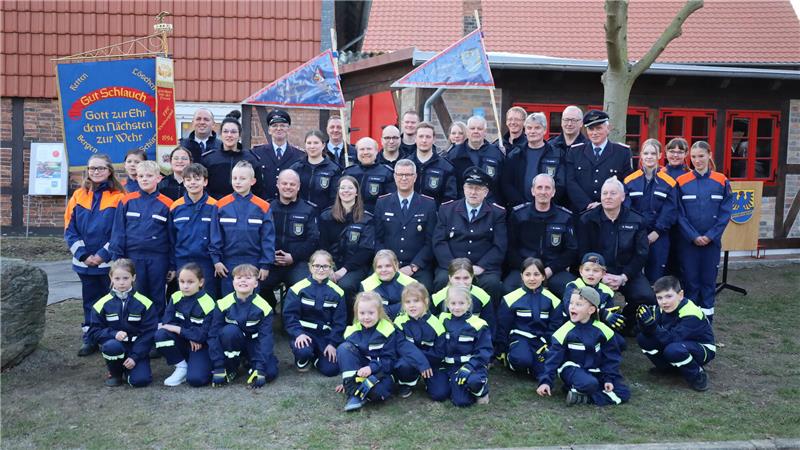 Pferdespritze nimmt ihren Platz im Kleinen Spritzenhaus ein Gruppenfoto von Feuerwehrleuten und Jugendfeuerwehrmitgliedern in Uniform vor einem Fachwerkhaus mit Fahnen