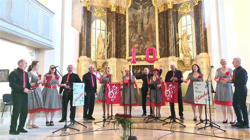 Ein Ensemble von Männern und Frauen steht vor einem Kirchenaltar und singt.