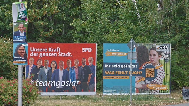 Zwei Wahlplakate an einer Straße, links SPD mit mehreren Personen und dem Text 'Unsere Kraft der ganzen Stadt. #teamgoslar', rechts CDU mit einer Frau, die einen Korb hält, und dem Text 'Ihr seid gefragt! WAS FEHLT EUCH?'.