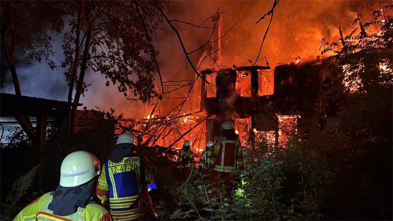 Feuerwehrleute in Schutzkleidung löschen ein brennendes Gebäude in der Nacht