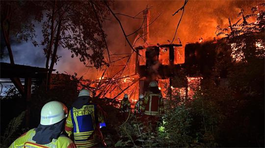 Feuerwehrleute in Schutzkleidung löschen ein brennendes Gebäude in der Nacht
