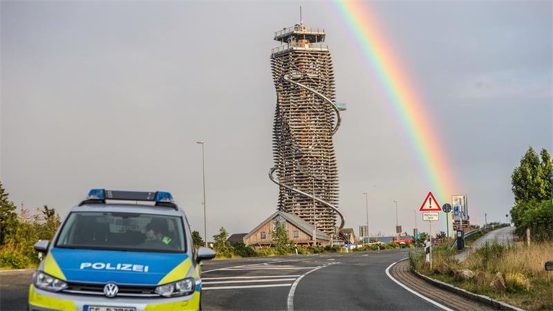 Harzturm neben einer Straße, im Hintergrund ein Regenbogen und ein Polizeiauto im Vordergrund