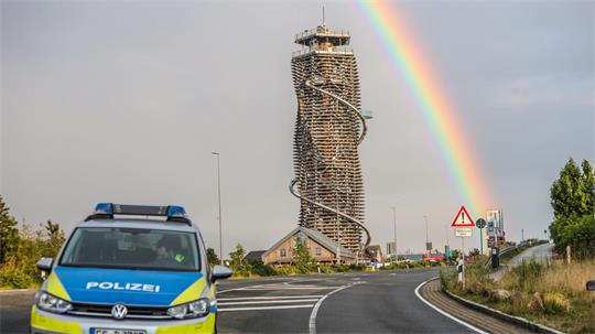 Harzturm neben einer Straße, im Hintergrund ein Regenbogen und ein Polizeiauto im Vordergrund