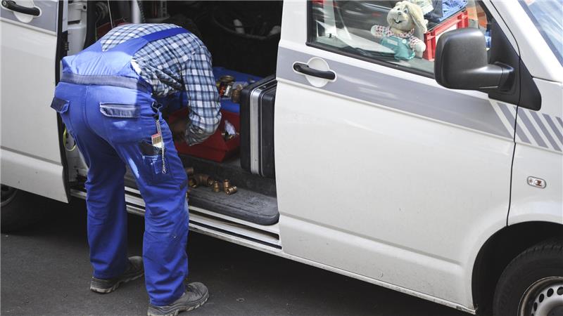 Ein Klempner holt seine Werkzeugtasche aus dem Auto.